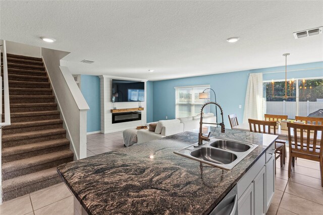 kitchen with a kitchen island with sink, sink, a fireplace, decorative light fixtures, and light tile patterned flooring