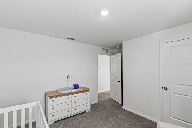 bedroom featuring a crib, a textured ceiling, and carpet floors