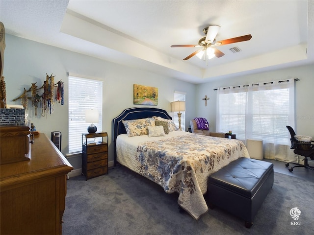 bedroom featuring a raised ceiling, ceiling fan, and dark carpet