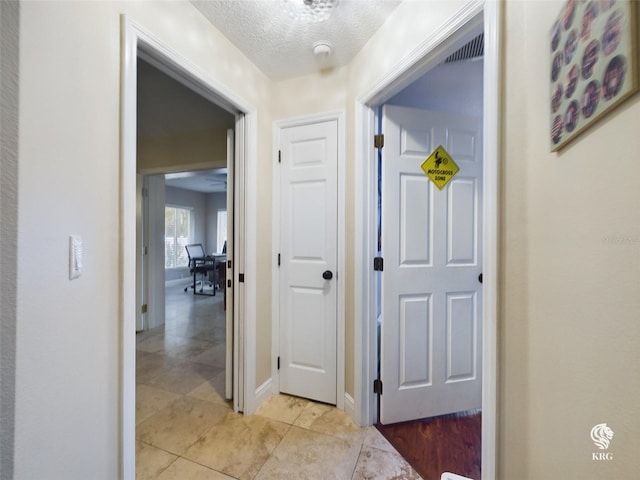 hall featuring light tile patterned floors and a textured ceiling