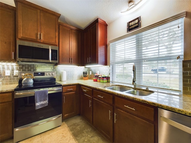 kitchen featuring sink, decorative backsplash, stainless steel appliances, light stone countertops, and a textured ceiling