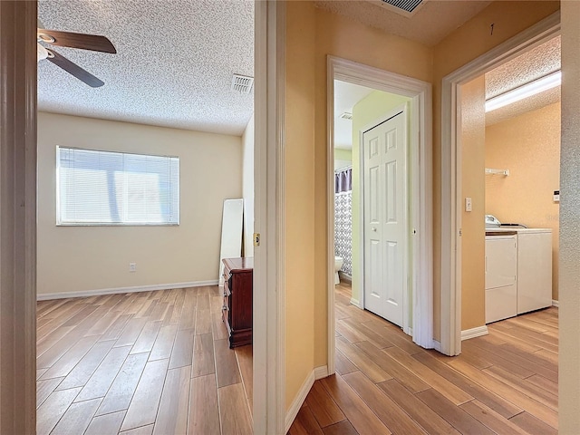 corridor with a textured ceiling, light hardwood / wood-style floors, and washing machine and clothes dryer