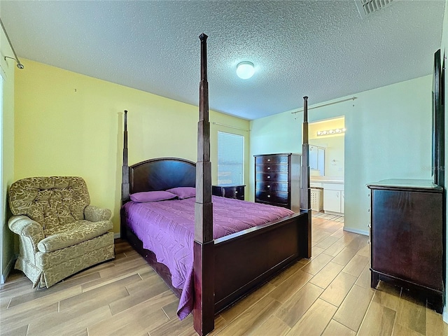 bedroom with a textured ceiling, connected bathroom, and light hardwood / wood-style floors