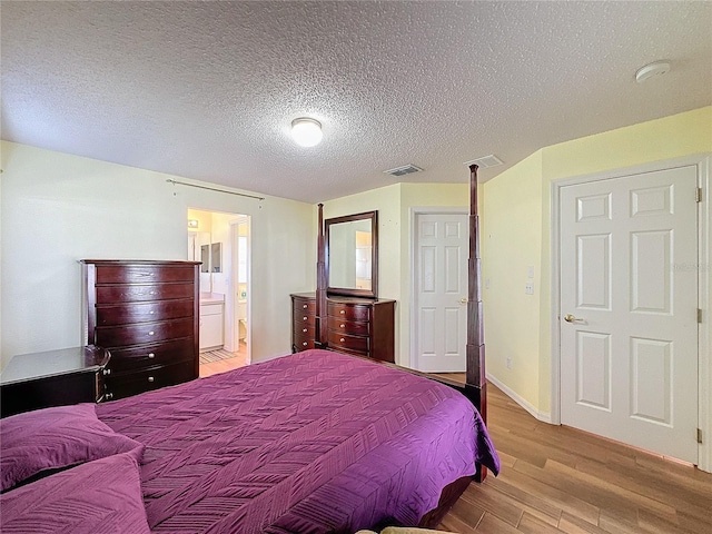 bedroom with a textured ceiling, connected bathroom, and light hardwood / wood-style flooring