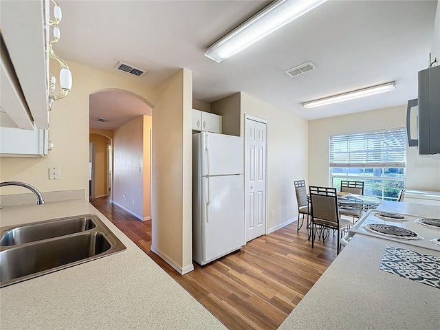 kitchen with sink, stove, white fridge, pendant lighting, and white cabinets