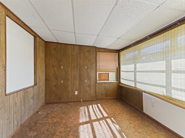 unfurnished room featuring wood walls and a drop ceiling