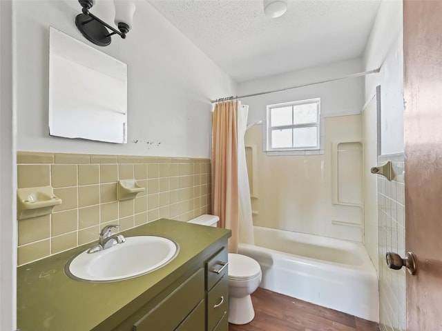 full bathroom featuring toilet, a textured ceiling, tile walls, shower / bath combo, and vanity