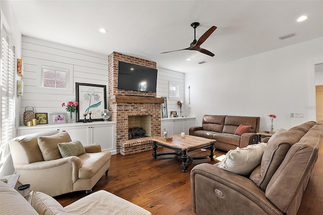 living room featuring dark hardwood / wood-style flooring, a brick fireplace, ceiling fan, and wooden walls