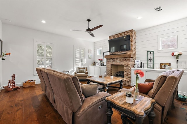 living room with a fireplace, dark hardwood / wood-style flooring, ceiling fan, and wooden walls