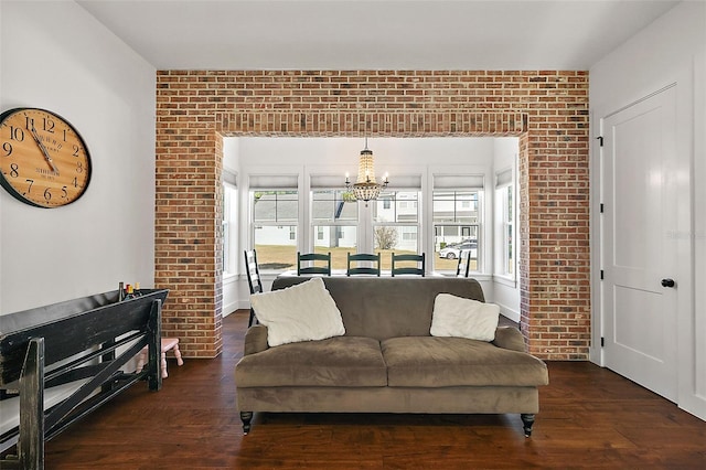 living room with dark wood-type flooring, brick wall, and a notable chandelier