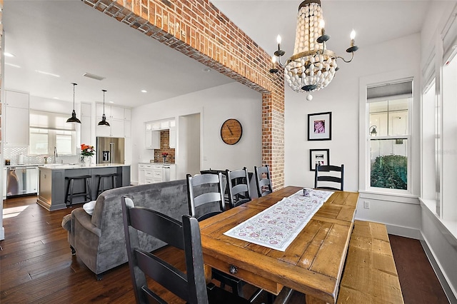 dining room with a notable chandelier, sink, dark wood-type flooring, and brick wall