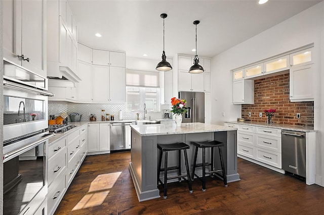 kitchen with white cabinetry, a center island, stainless steel appliances, tasteful backsplash, and light stone counters