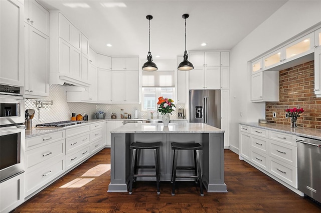 kitchen with dark wood-type flooring, white cabinets, a kitchen island, light stone counters, and stainless steel appliances