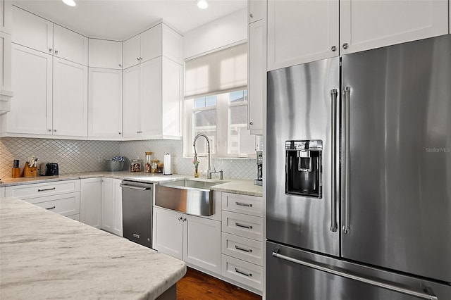 kitchen featuring sink, stainless steel appliances, tasteful backsplash, light stone counters, and white cabinets