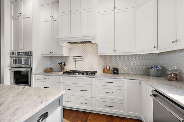 kitchen featuring light stone countertops, dark wood-type flooring, decorative backsplash, white cabinets, and appliances with stainless steel finishes