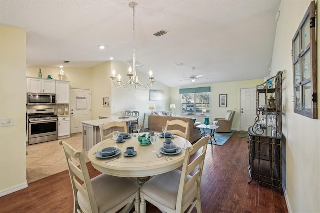 dining space featuring ceiling fan with notable chandelier, hardwood / wood-style flooring, and vaulted ceiling