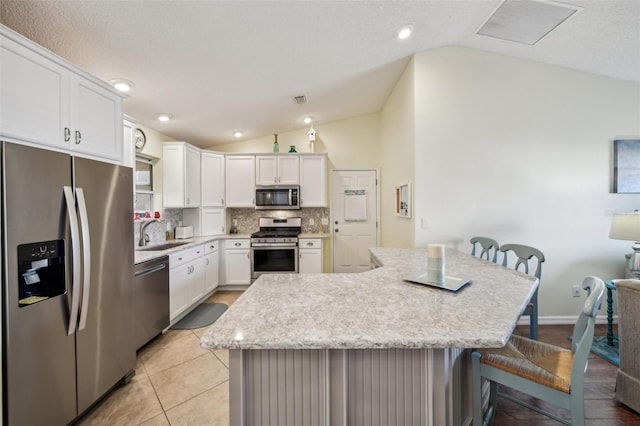 kitchen featuring a kitchen breakfast bar, white cabinetry, stainless steel appliances, and lofted ceiling