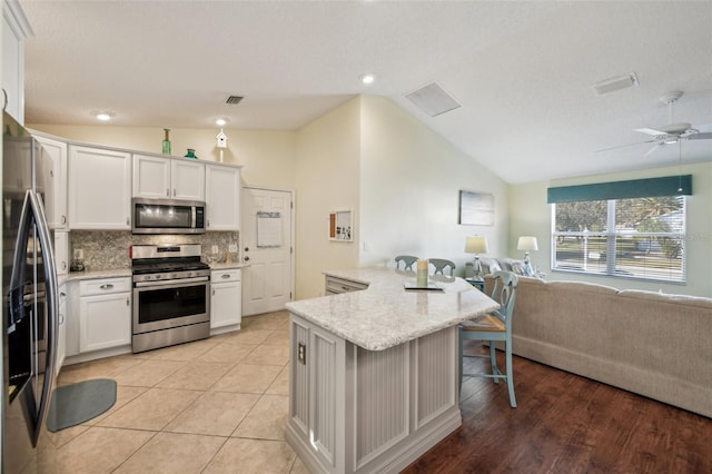 kitchen featuring a kitchen bar, appliances with stainless steel finishes, backsplash, vaulted ceiling, and white cabinets