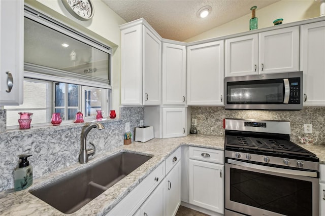 kitchen featuring sink, lofted ceiling, decorative backsplash, white cabinets, and appliances with stainless steel finishes