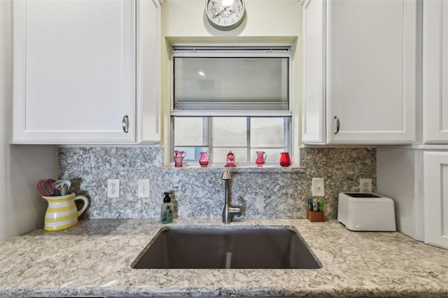 kitchen with tasteful backsplash, white cabinetry, sink, and light stone counters