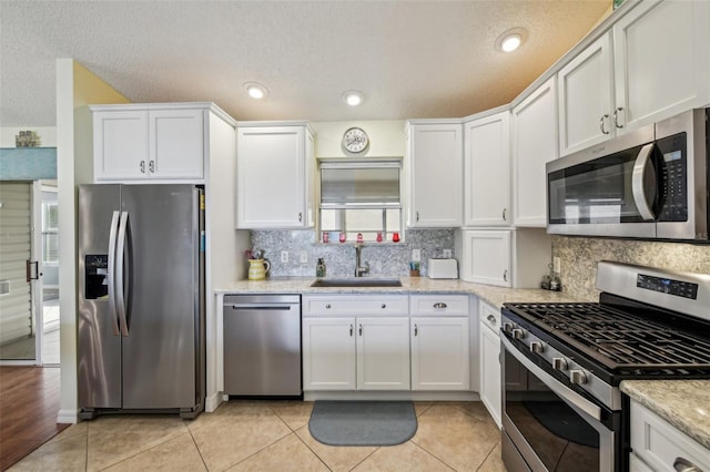 kitchen featuring white cabinets, sink, light tile patterned floors, appliances with stainless steel finishes, and light stone counters