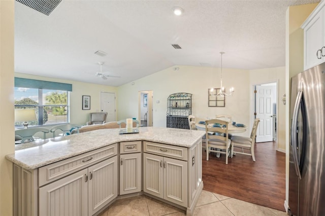 kitchen with pendant lighting, ceiling fan with notable chandelier, vaulted ceiling, light tile patterned flooring, and stainless steel refrigerator