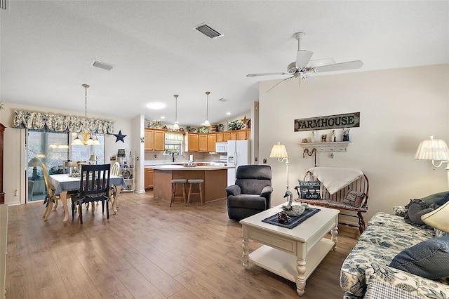 living room with ceiling fan with notable chandelier, wood-type flooring, a textured ceiling, and vaulted ceiling