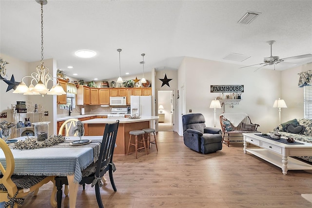 dining area with ceiling fan with notable chandelier, vaulted ceiling, and light wood-type flooring