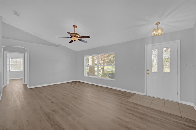 foyer entrance featuring ceiling fan with notable chandelier, wood-type flooring, a wealth of natural light, and vaulted ceiling