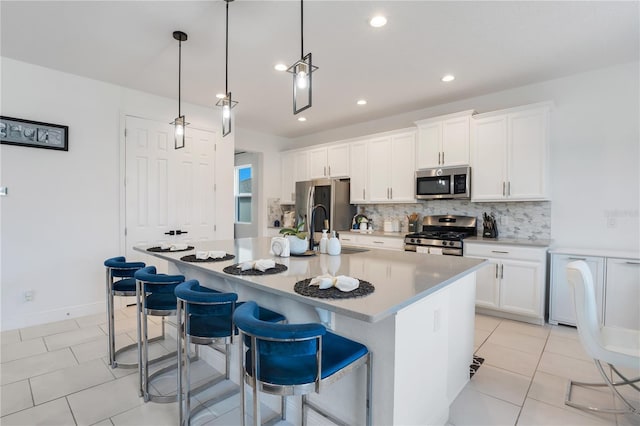 kitchen with hanging light fixtures, an island with sink, a kitchen bar, white cabinets, and appliances with stainless steel finishes