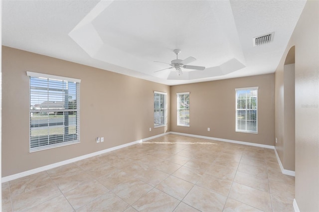 tiled spare room featuring a raised ceiling, a wealth of natural light, and ceiling fan