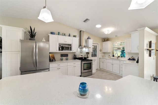 kitchen featuring sink, wall chimney range hood, pendant lighting, white cabinets, and appliances with stainless steel finishes