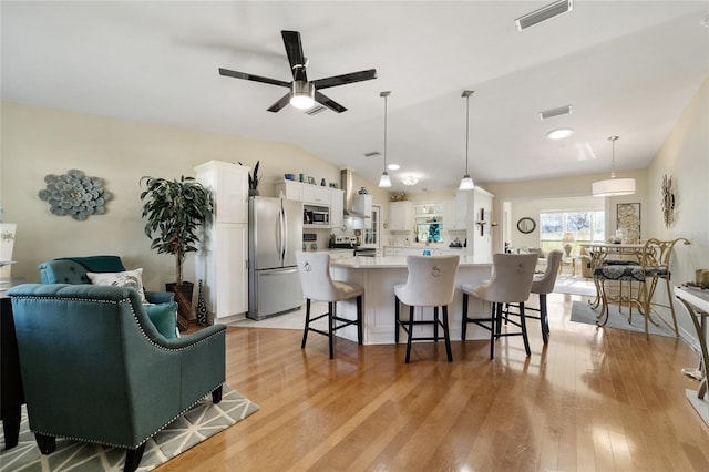 kitchen with a breakfast bar, white cabinets, decorative light fixtures, light hardwood / wood-style floors, and stainless steel appliances