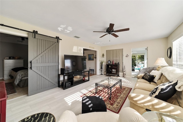 living room with a barn door, light hardwood / wood-style flooring, and ceiling fan