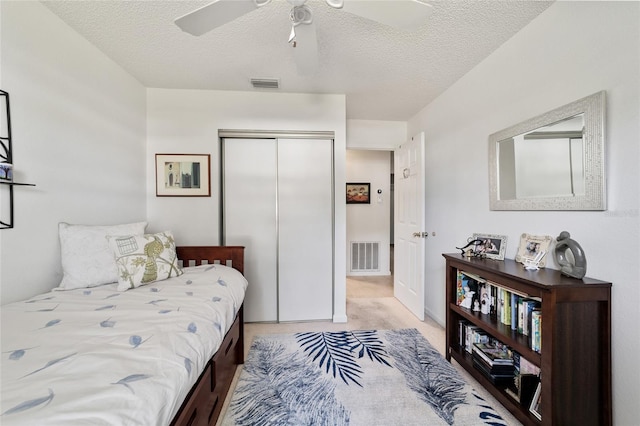 carpeted bedroom with ceiling fan, a closet, and a textured ceiling