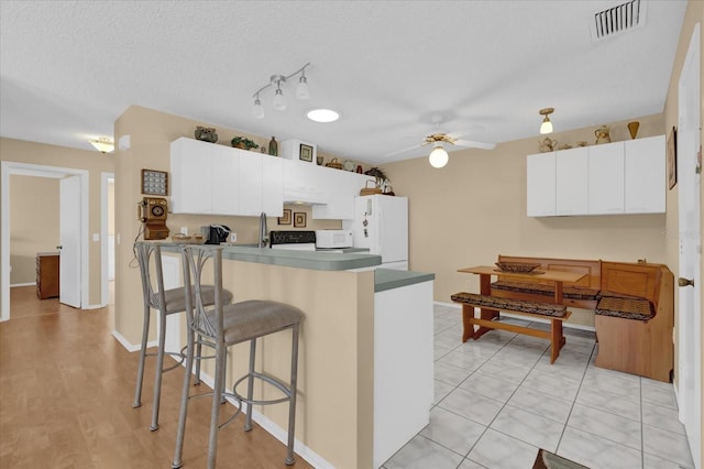 kitchen featuring a textured ceiling, white appliances, ceiling fan, light tile patterned floors, and white cabinets