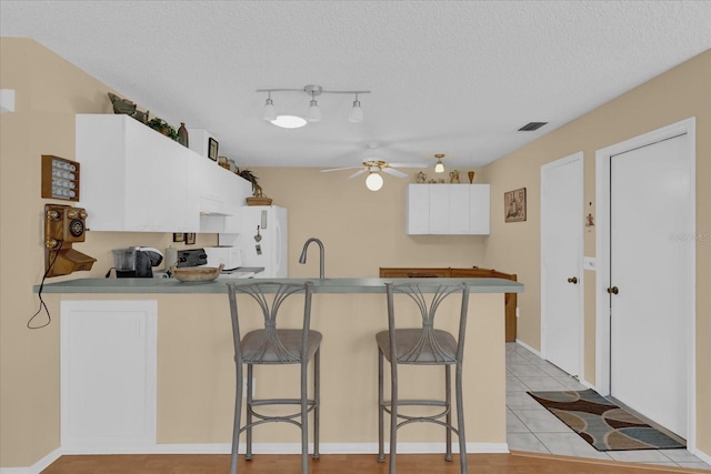 kitchen with a breakfast bar area, kitchen peninsula, white cabinets, and a textured ceiling