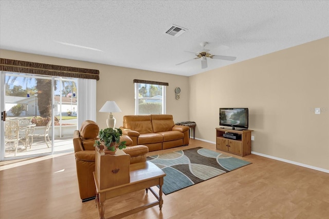 living room featuring ceiling fan, a healthy amount of sunlight, a textured ceiling, and light wood-type flooring