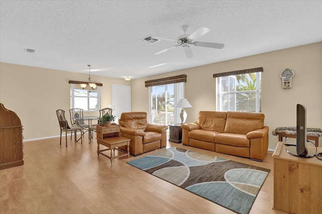 living room with a textured ceiling, light hardwood / wood-style flooring, a healthy amount of sunlight, and ceiling fan with notable chandelier