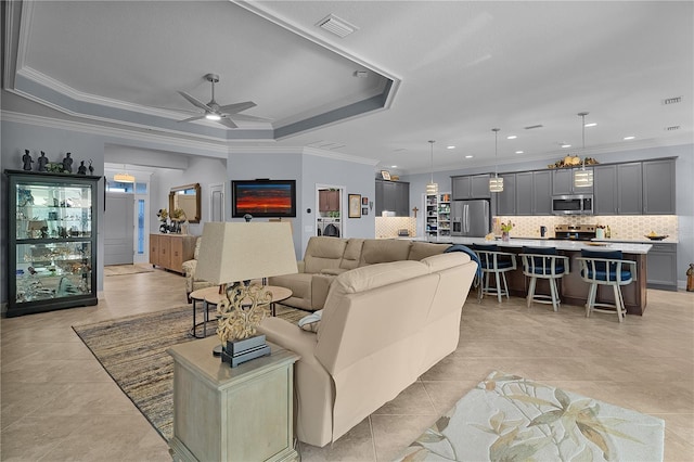 living room featuring ceiling fan, light tile patterned floors, a tray ceiling, and crown molding