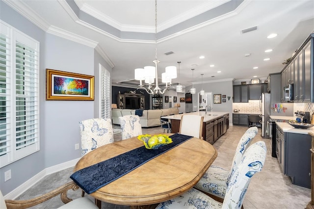 dining space featuring a tray ceiling, sink, an inviting chandelier, and ornamental molding