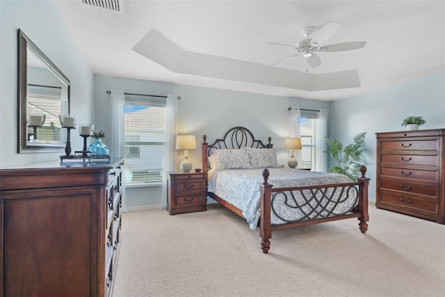 bedroom with ceiling fan, light colored carpet, and a tray ceiling