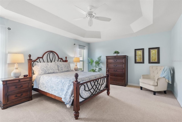 carpeted bedroom with a raised ceiling and ceiling fan