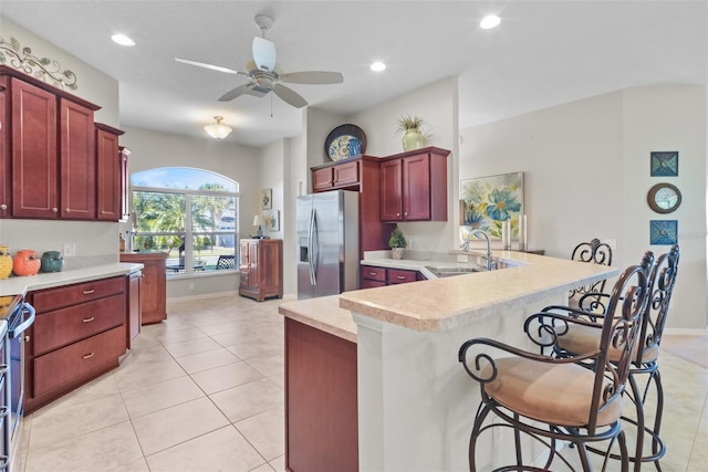 kitchen with ceiling fan, sink, stainless steel fridge with ice dispenser, a breakfast bar, and light tile patterned floors