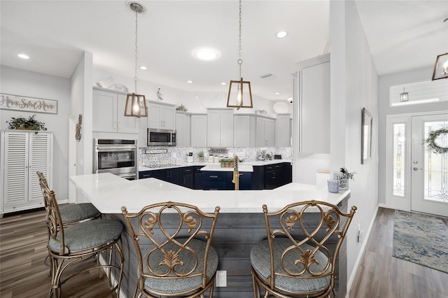 kitchen with stainless steel appliances, kitchen peninsula, a breakfast bar area, backsplash, and pendant lighting