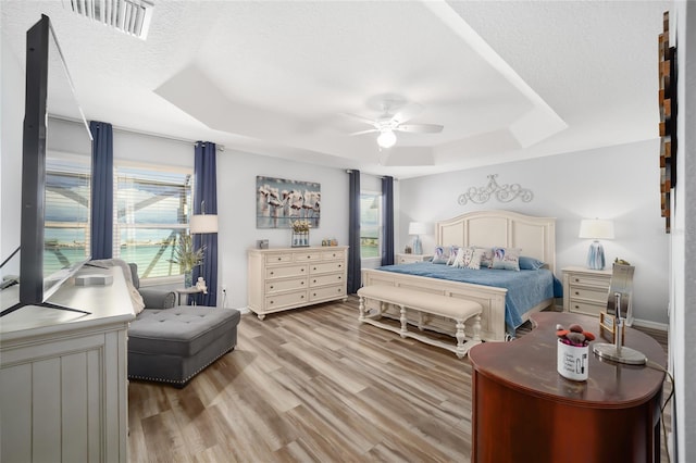 bedroom featuring ceiling fan, multiple windows, and a tray ceiling