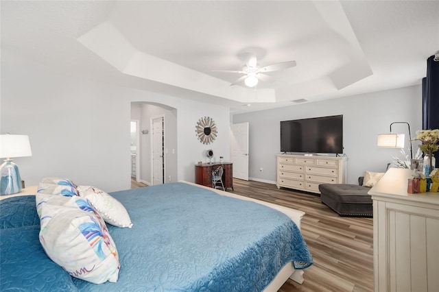 bedroom featuring ceiling fan, hardwood / wood-style floors, a raised ceiling, and connected bathroom