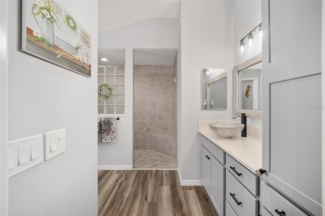 bathroom featuring tiled shower, lofted ceiling, vanity, and wood-type flooring