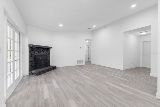 unfurnished living room featuring light hardwood / wood-style floors, a stone fireplace, and a healthy amount of sunlight