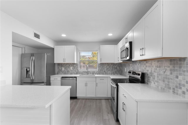 kitchen with backsplash, stainless steel appliances, sink, white cabinets, and light hardwood / wood-style floors